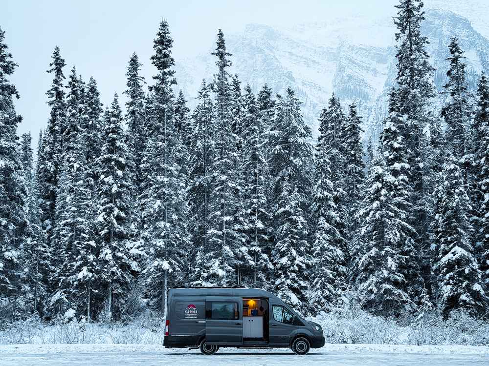 Campervan with lights on beneath snowy evergreens