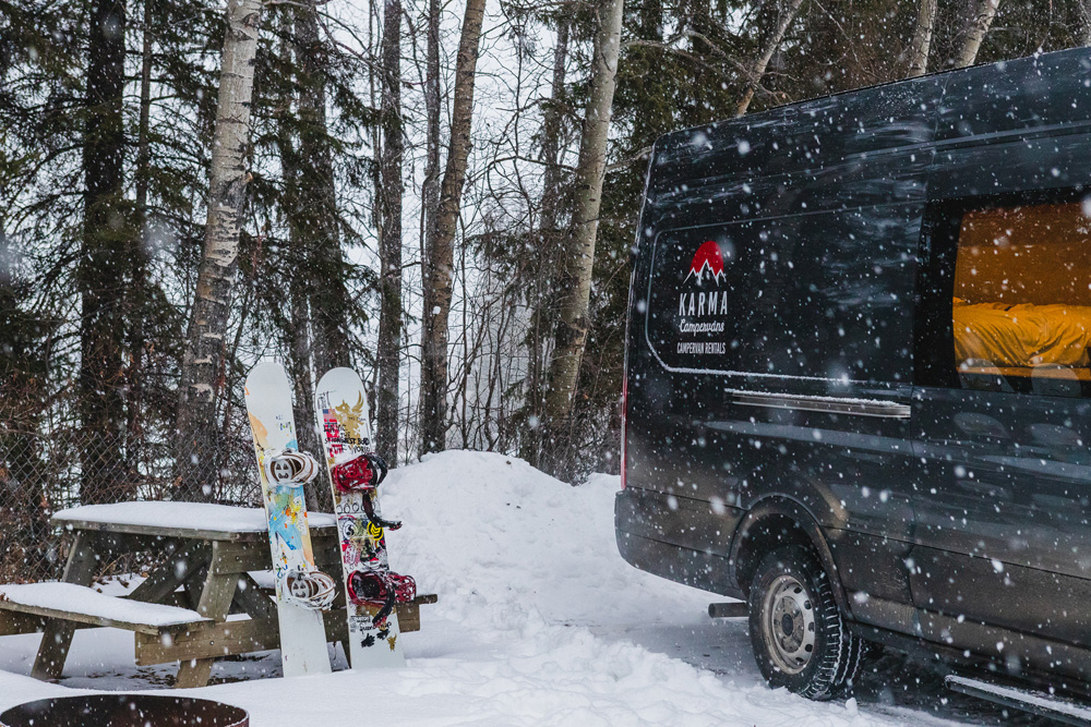 Snowboards beside a Karma Campervan at a snowy campsite